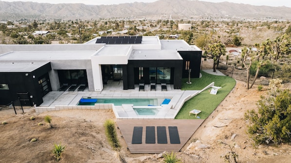 A modern house with a swimming pool, outdoor seating, and a view of the surrounding landscape.