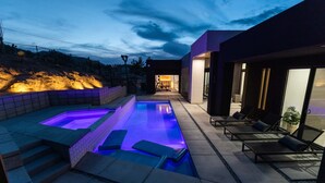 A modern outdoor pool area with a rectangular pool and a separate hot tub, surrounded by a patio with seating and a view of a hillside. - Joshua Tree Hot Tub, Pool, Gym & Fireplace (Yucca Valley)