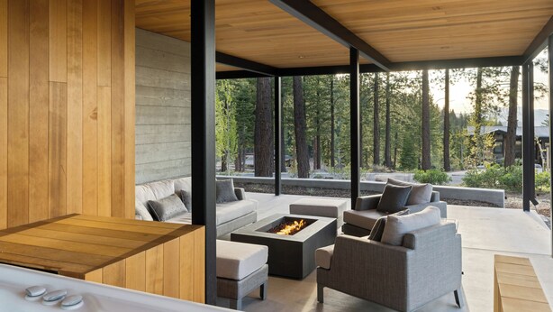 Un espace moderne aménagé à l’extérieur avec un jacuzzi, une terrasse en bois, des canapés gris et un foyer.