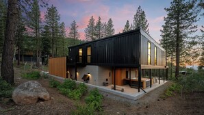 Une maison moderne à deux étages, dotée d’une terrasse en bois et d’un grand rocher au premier plan.
