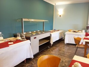 A buffet setup with multiple serving stations, a beverage dispenser, and a seating area with tables and chairs. - Hotel Acquamaris 3000 (Sanxenxo)