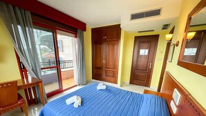 A hotel room with a bed, a desk, a chair, a balcony, and a door.