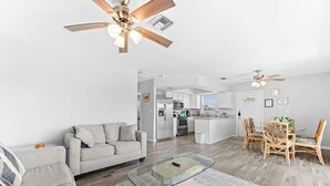 A modern living room with a sofa, a glass coffee table, and a dining area with chairs. - Huge Shared Pool, Walk to Beach, Times Square Restaurants! (Fort Myers Beach)