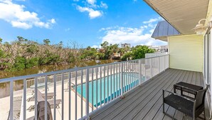 A wooden deck with a pool, white railings, and outdoor furniture. - Huge Shared Pool, Walk to Beach, Times Square Restaurants! (Fort Myers Beach)