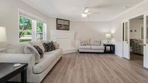 A living room with a white sofa, a gray sofa, a wooden floor, and a ceiling fan. - Spacious Dog Friendly Home w/ Full Sized Pool - Game Room In Garage- 3BR, 2BTH, (Oak Island)