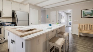 A kitchen with white cabinets, a large island, and a dining area with a bench. - Spacious Dog Friendly Home w/ Full Sized Pool - Game Room In Garage- 3BR, 2BTH, (Oak Island)