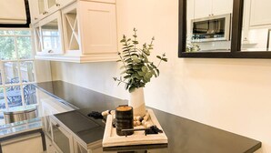 Una cocina con armarios blancos, encimera negra, una planta en maceta, una bandeja con una vela y un vaso de agua.