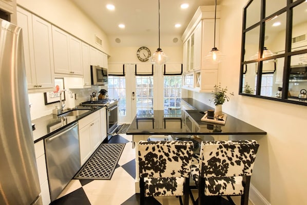Una cocina moderna con armarios blancos, encimera negra y dos sillas con estampado de vaca.