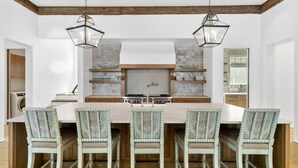A modern kitchen with a central island, wooden beams, hanging pendant lights, and a tiled backsplash.