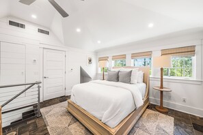 Une chambre à coucher avec un lit, une lampe sur pied, une fenêtre avec des stores, une porte et un escalier.