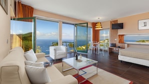 Een moderne hotelkamer met een ruim balkon, een bank, een bijzettafeltje en een televisie.