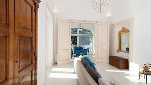 A spacious room with a large wooden wardrobe, a sofa with blue and grey cushions, a chandelier, and a view through a large window. - Splendid luxury villa, an ancient palace in Amalfi with jacuzzi-pool and sea-view, at 300 m from the (Amalfi)