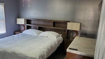 A bedroom with a bed, a nightstand, a desk, a ceiling fan, and a wall-mounted lamp.
