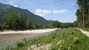 Een rivier met een grindpad ernaast, omgeven door groen en bergen.