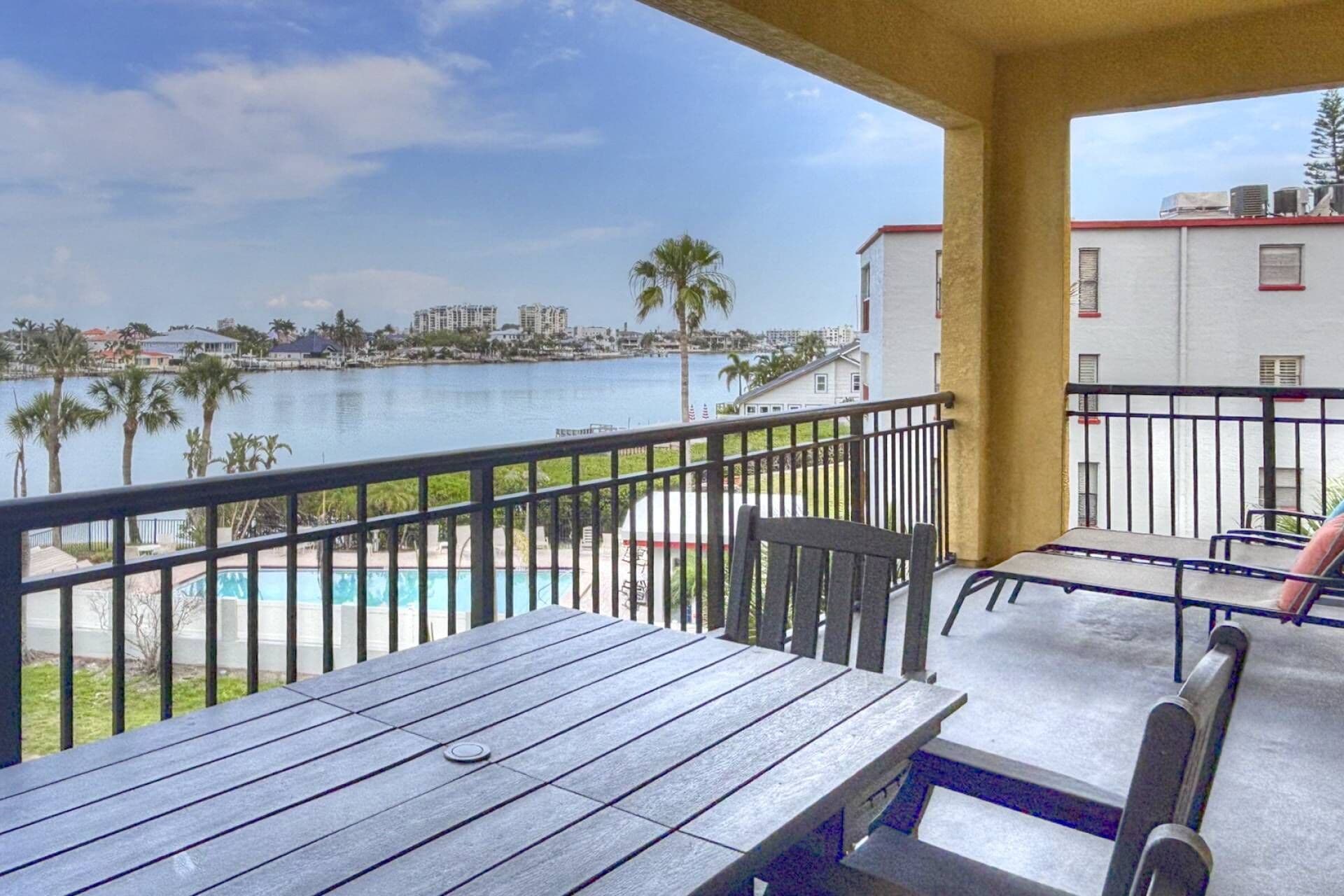 A balcony with a view of a swimming pool, palm trees, and a distant cityscape.