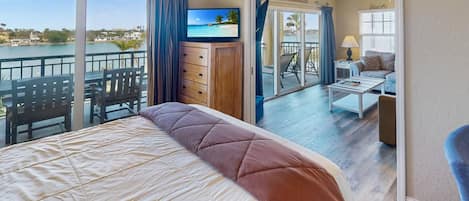 Habitación de hotel con cama, televisión, balcón con vista al mar y zona de estar con mesa y sillas.