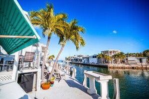 A marina with boats docked, a palm tree, and a building with a balcony. - Mile Marker Mahi - Venture Out #465 (Cudjoe Key)