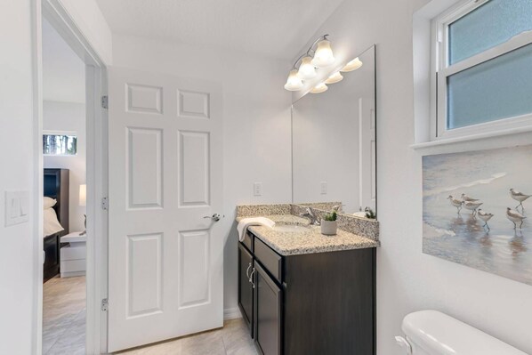 A modern bathroom with a granite countertop, dark cabinetry, and a large mirror.