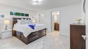 A bedroom with a bed, bedside tables, a dresser, and a bathroom visible through an open door.