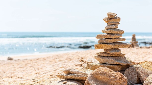 A stack of stones on a sandy beach with the ocean in the background.