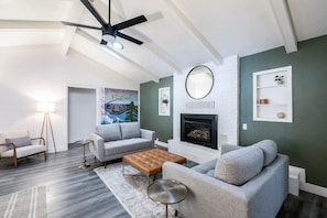 A modern living room with a fireplace, grey sofas, a coffee table, and a ceiling fan.