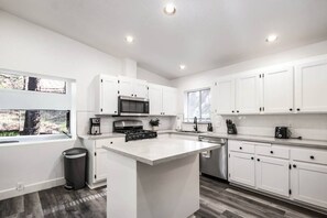 A modern kitchen with white cabinetry, a central island, stainless steel appliances, and a window providing natural light.