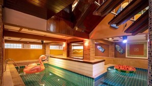 Una piscina interior con techo de madera, un flotador con forma de flamenco rosa y un flotador de sandía.