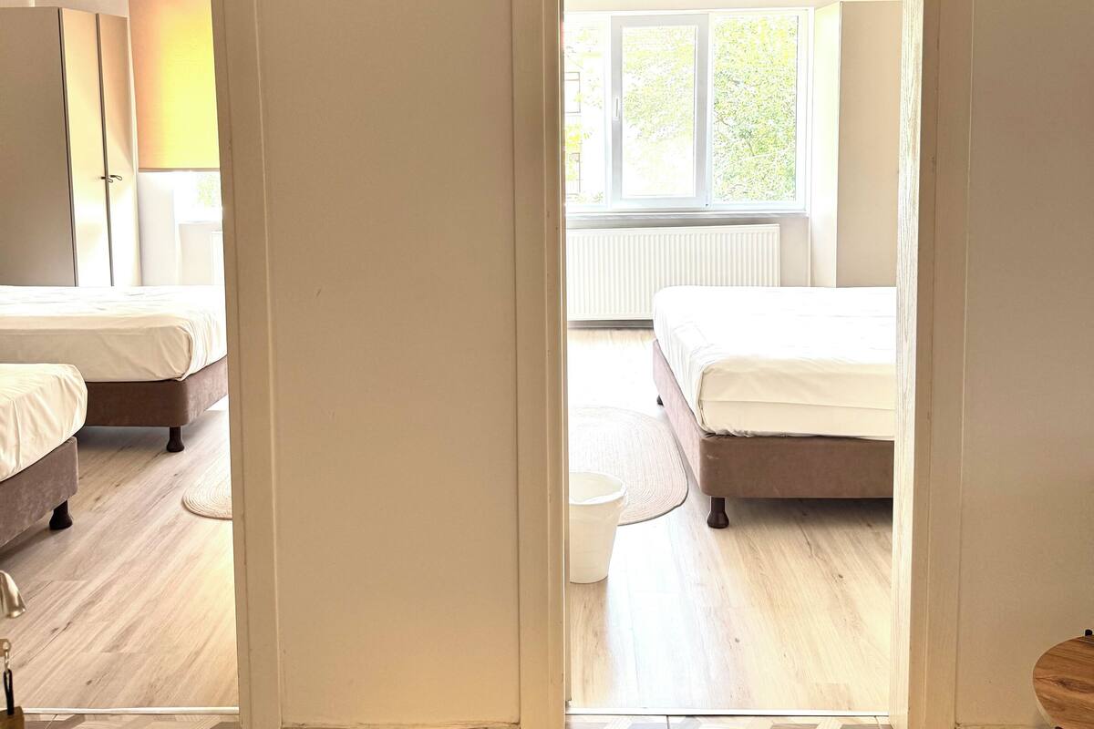 Una habitación con dos camas, piso de madera y vista a otra habitación por una puerta abierta.