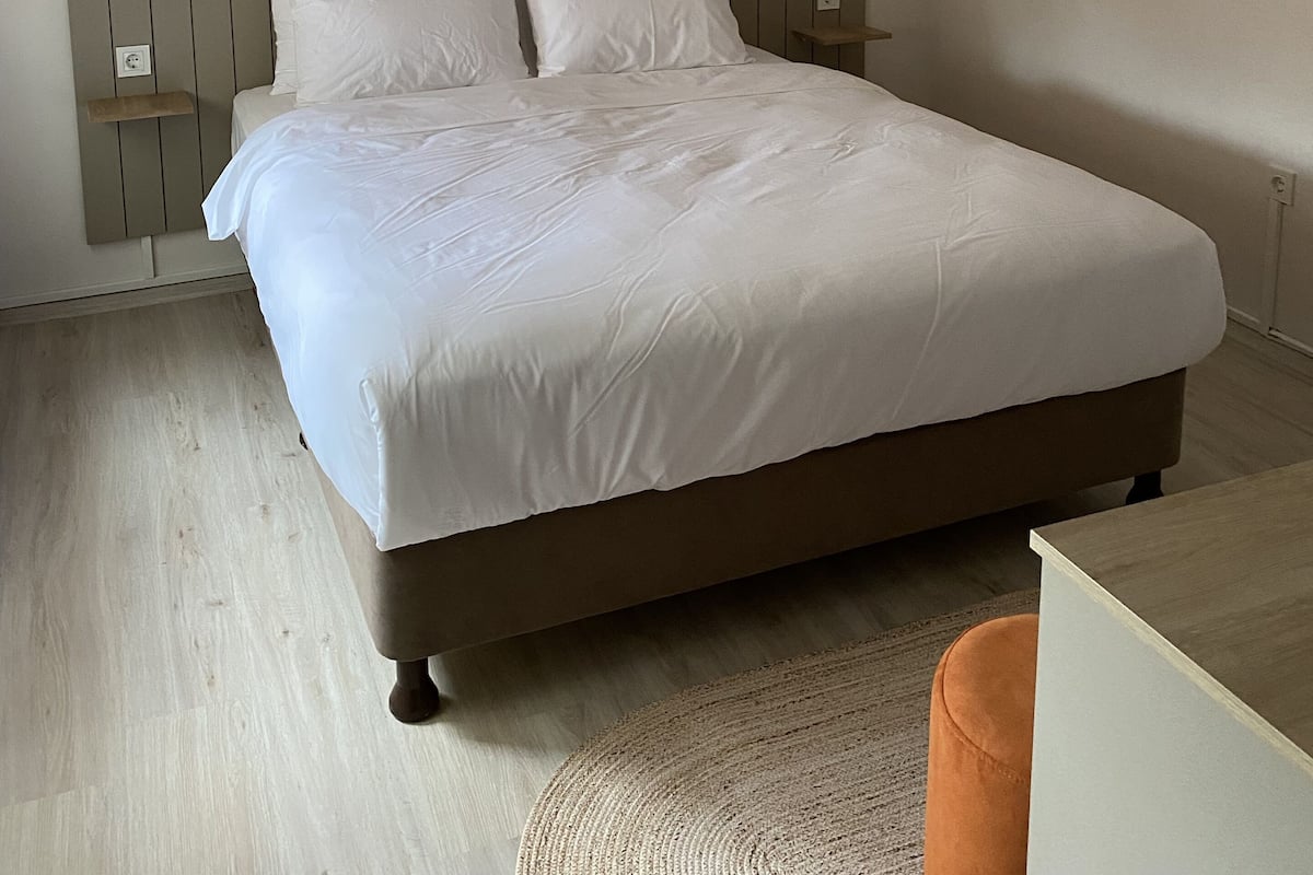 Una cama bien tendida con sábanas blancas, un cabecero de madera y una mesita de noche con una lámpara.