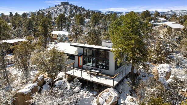 A modern house with a glass facade, situated on a snowy mountain with a view of other houses and a hill in the background. - Mid Century Modern home in the boulders. Amazing views. 1 mile from downtown. (Prescott)