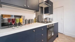 Moderni keittiö, jossa on tummat kaapit, sisäänrakennettu uuni sekä työtaso, jossa on erilaisia keittiökoneita ja lasiesineitä.