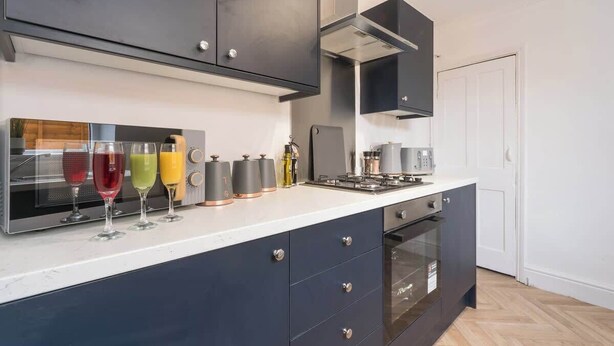 Een moderne keuken met donkere kastjes, een inbouwoven en een aanrecht met diverse keukenapparaten en glazen.