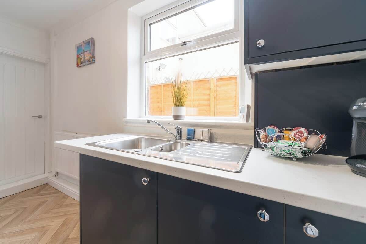 A kitchen with a double sink, a window with a view of a wooden fence, and a potted plant on the windowsill.