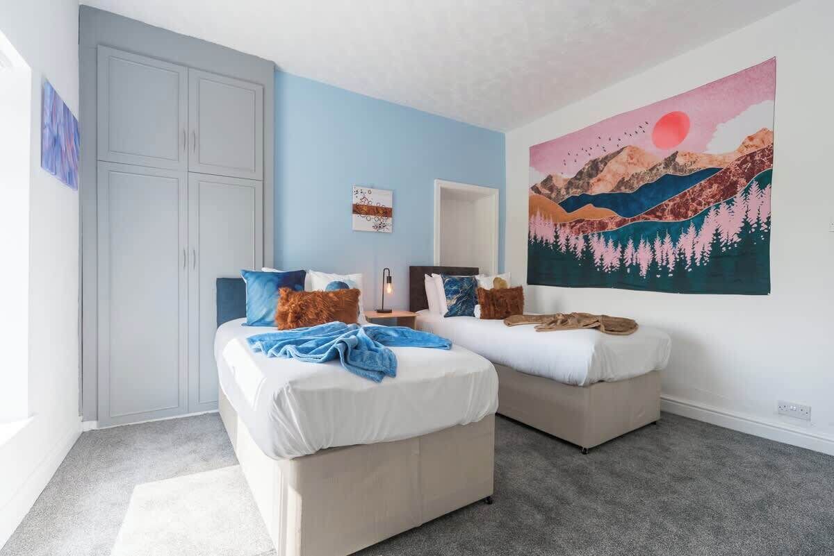A bedroom with two beds, a wardrobe, a painting, and a carpeted floor.