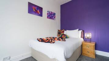 Una camera da letto con un letto, un comodino e una parete decorata con due opere d'arte.