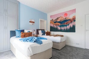A bedroom with two beds, a large painting of a landscape, and a wardrobe.