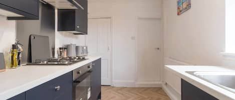 A kitchen with a gas stove, oven, and cabinets. There is a door and a painting on the wall.