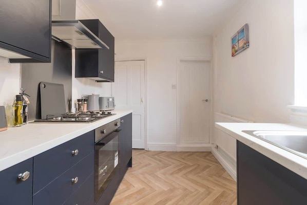 A kitchen with a gas stove, oven, and cabinets. There is a door and a painting on the wall.