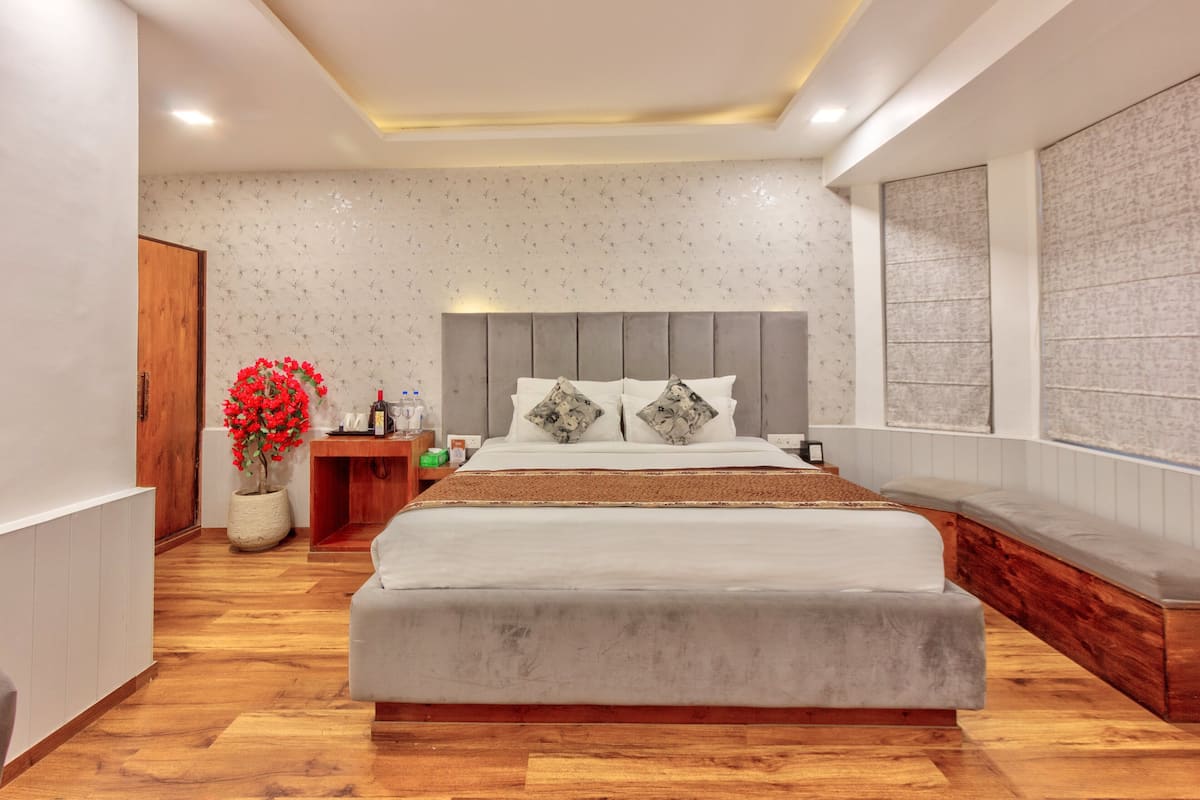 A modern bedroom with a large bed, a wooden floor, a wooden nightstand, a potted plant, and a large window.