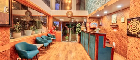 A modern hotel lobby with wooden flooring, blue chairs, a reception desk, and a large mirror.