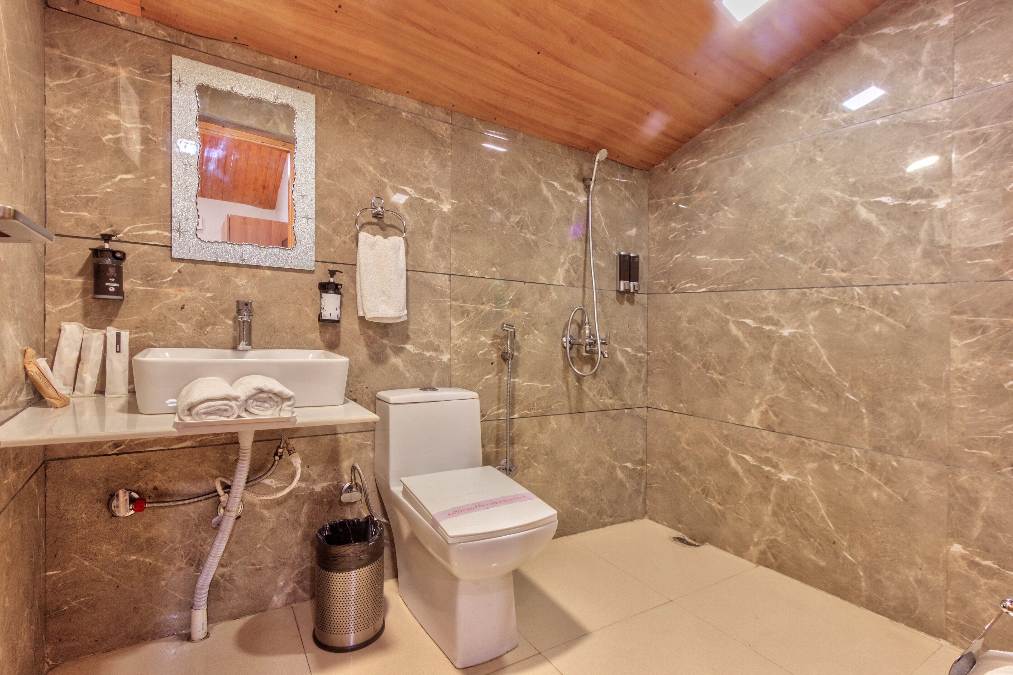 A bathroom with a marble wall, a wooden ceiling, a sink, a toilet, and a shower.