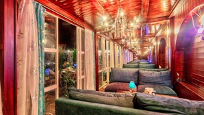 A corridor with green upholstered seating, a chandelier, and large windows. - PARADISE - The Whitehouse Cafe (Manali)