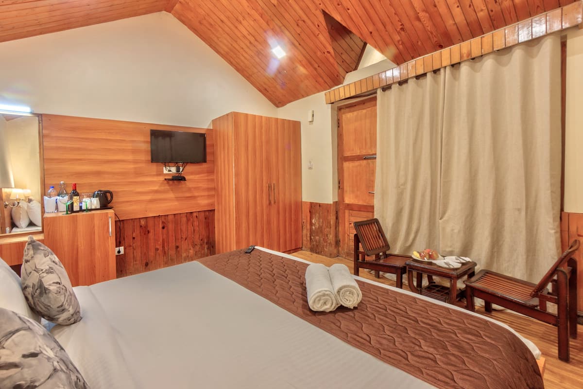 A hotel room with a wooden ceiling, a bed with rolled towels, a television on the wall, and a dining area with a table and chairs.