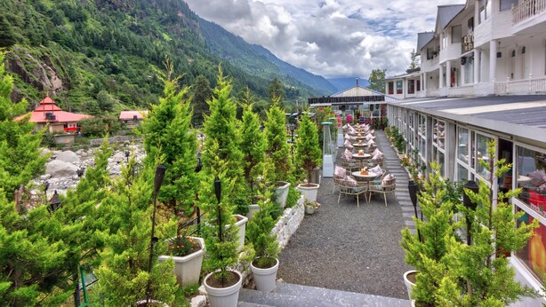 A hotel with outdoor seating and potted trees, overlooking a mountainous area. - PARADISE - The Whitehouse Cafe (Manali)