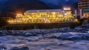 A hotel with a multi-story structure, a visible restaurant, and a river in the foreground. - PARADISE - The Whitehouse Cafe (Manali)