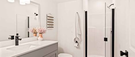 Un baño moderno con lavamanos blanco, inodoro y ducha con mampara de vidrio.