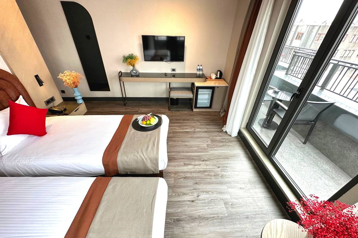 Une chambre d’hôtel avec deux lits, un bureau doté d’une télévision à écran plat, un petit réfrigérateur et un balcon avec vue.