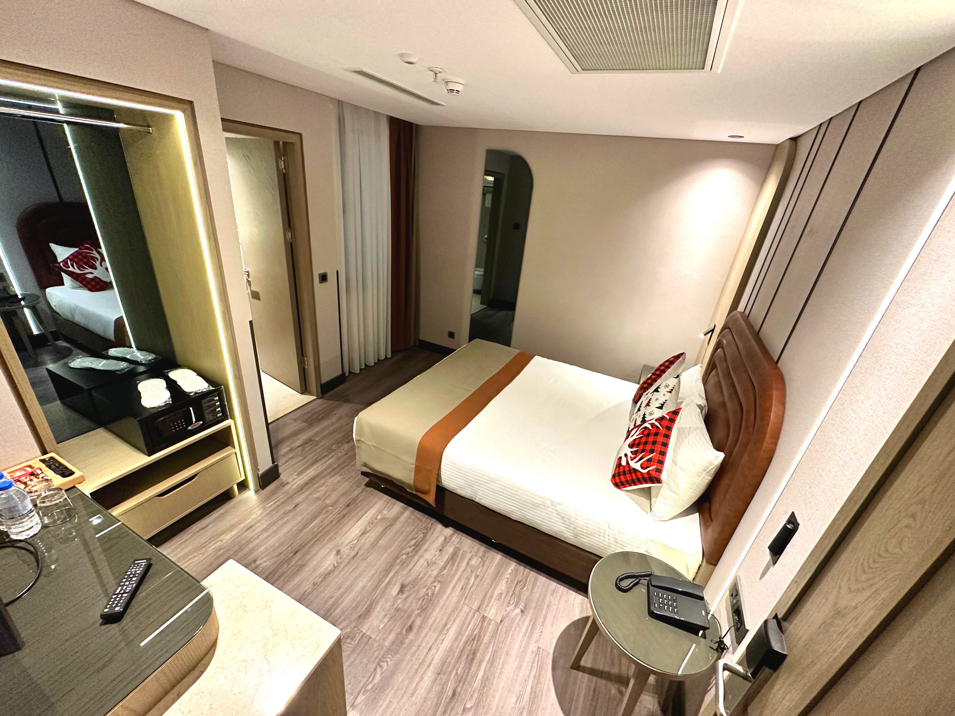 A hotel room with a bed, bedside table, mirror, and a small round table with a phone.