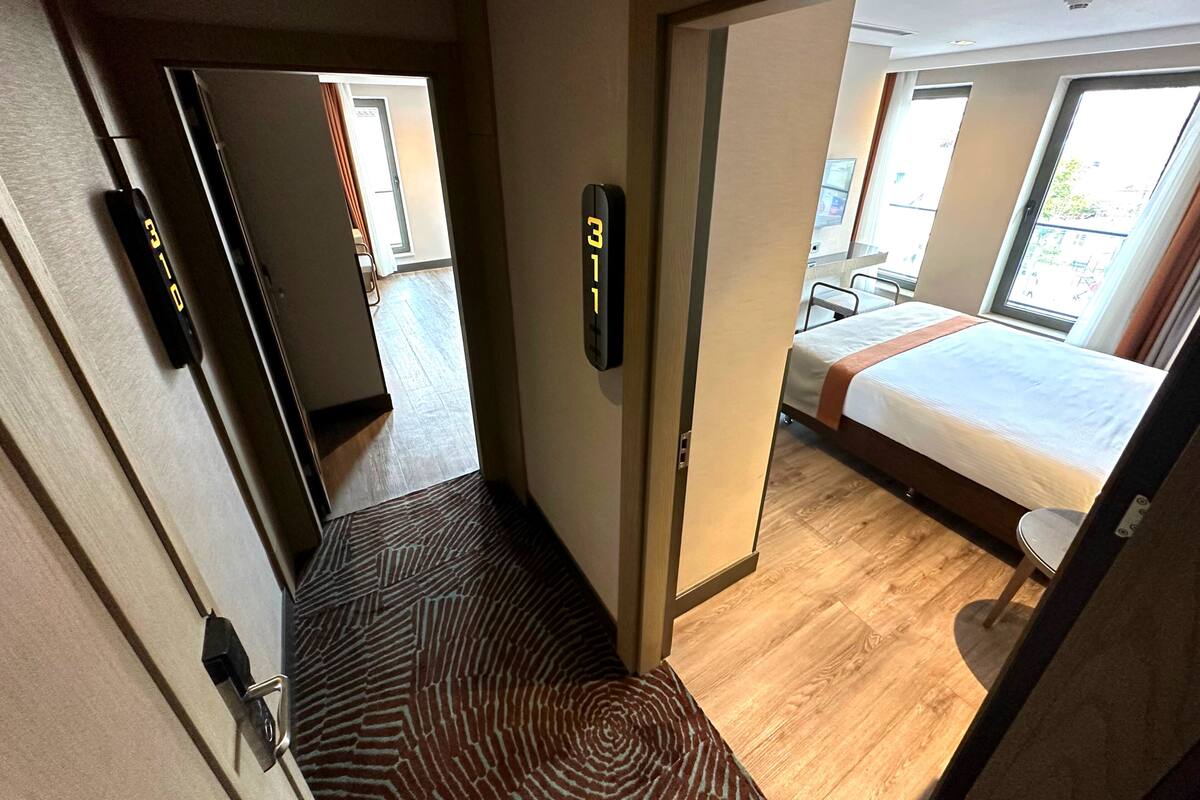 Une chambre d’hôtel avec un lit, une chaise et une salle de bain, visibles à travers une porte ouverte.