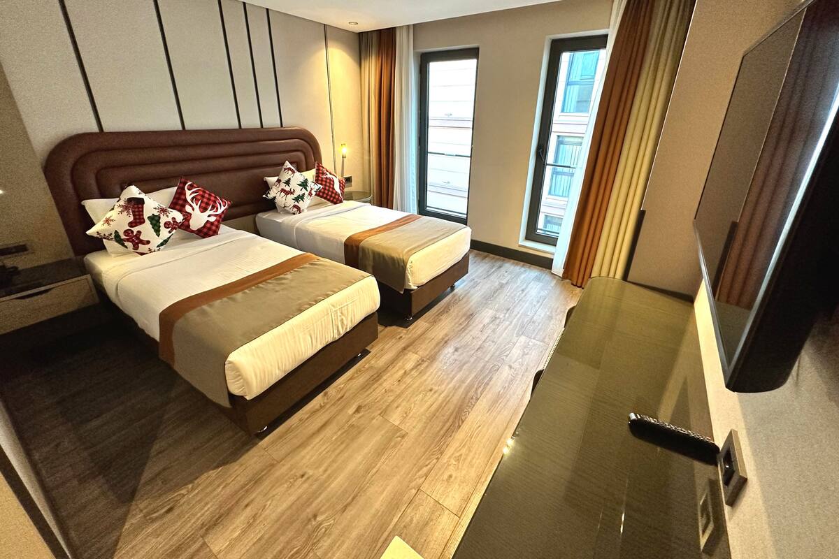 Une chambre d’hôtel avec deux lits, un téléviseur à écran plat, un plancher en bois et une grande fenêtre avec des rideaux.